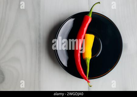 One and a half hot peppers on a black round plate. Light background. White boards. Spices in the kitchen. Stock Photo