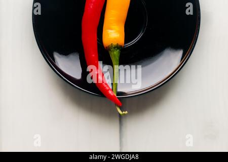One and a half hot peppers on a black round plate. Light background. White boards. Spices in the kitchen. Stock Photo