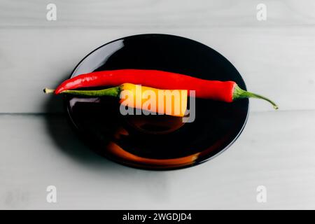 One and a half hot peppers on a black round plate. Light background. White boards. Spices in the kitchen. Stock Photo