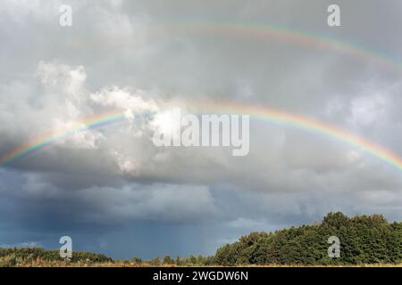Double rainbow over Lithuanian meadows and forest at cloudy day. Stock Photo