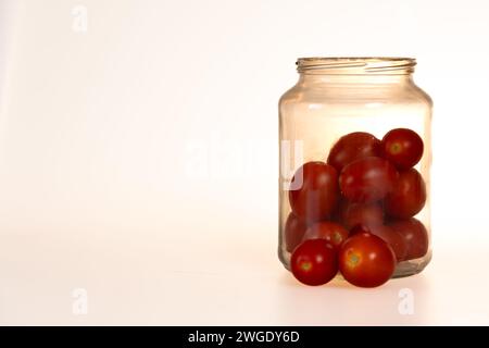 plum tomatoes in a glass jar, two tomatoes out of the jar on white background Stock Photo