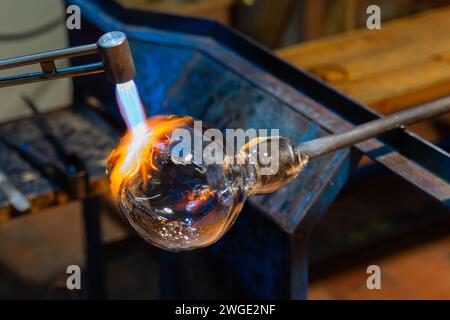 Creating glass art with hot torch and glassblowing pipe. The process of glass making.  Glassblower shaping the red melted glass. Stock Photo