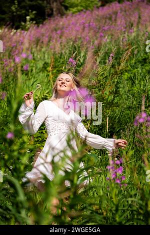 Young beautiful brunette woman walking through wildflowers in alpine meadow, summer dress, mountain, sunlight, wanderlust, happiness Stock Photo