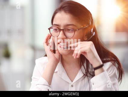 Portrait of a young woman in a headset working in an office center online from a laptop. Stock Photo