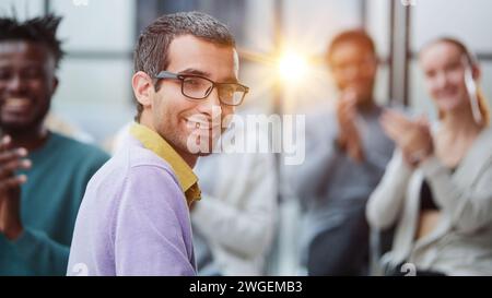 a man in casual clothes with glasses looks at the camera while sitting together with his colleagues Stock Photo