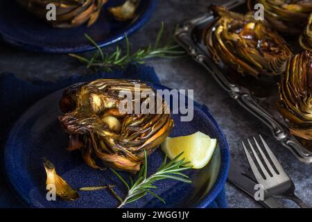 Roasted artichokes with garlic, rosemary and lemon on table - dark and moody photography Stock Photo