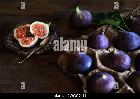 Cut fresh fig fruits on a small plate on wooden board with group figs in paper package - dark and moody photography Stock Photo