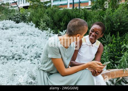 Joyful Moment Between Two Businesswomen Sharing Laughter in a Lush Urban Garden Stock Photo