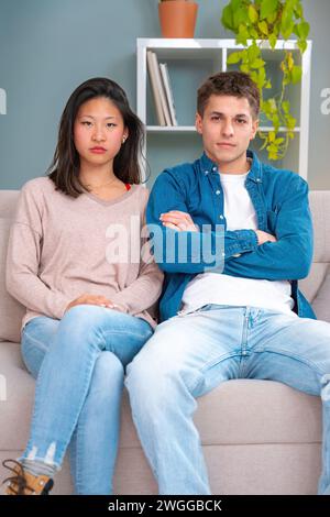 Vertical Portrait of young serious multiethnic couple using smartphone technology.Indoors Stock Photo