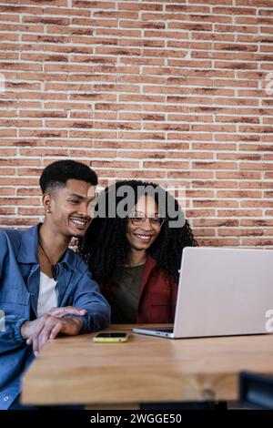 Friendly young adult woman and man in love watching at the computer screen. Happy young diverse couple sitting at living room having laptop video call Stock Photo