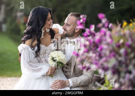 Portrait of newlyweds in love sitting together on a park bench. Stock Photo
