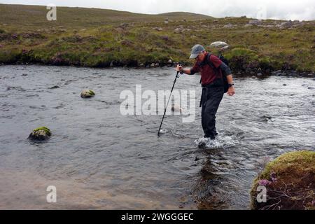 Man (Hiker) Wading River on the Outflow of 'Loch na h-Oidhche' in the Flowerdale Forest, Wester Ross, North West Highlands, Scotland, UK Stock Photo