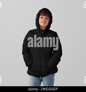 Mockup of black winter kids puffer jacket on hooded girl, front view, isolated on background in studio. Fashionable streetwear template with zipper, w Stock Photo