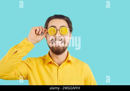 Cheerful funny hipster man in summer glasses in shape of orange slices on turquoise background. Stock Photo