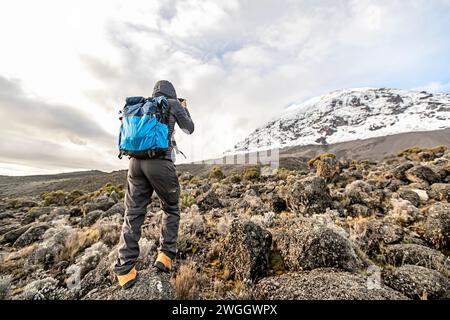 Hiker photographing view of snow-covered summit of Mount Kilimanjaro, Tanzania Stock Photo