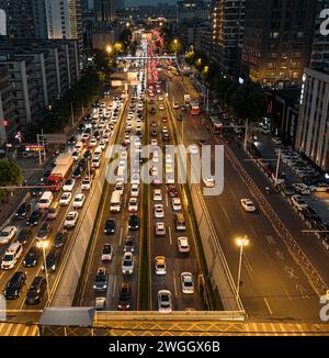 The intersection during the evening rush hour is filled with vehicles. Above the intersection is a pedestrian overpass Stock Photo