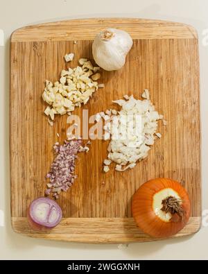 Wooden cutting board with onion, shallot and garlic bulb Stock Photo