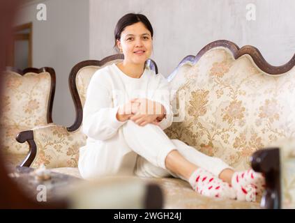 Relaxed young brunette sitting on soft antique sofa at home Stock Photo