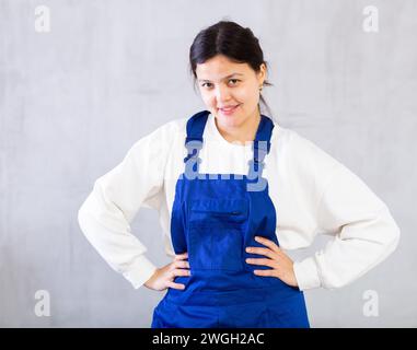 Smiling young female mechanic in blue overalls posing in studio Stock Photo
