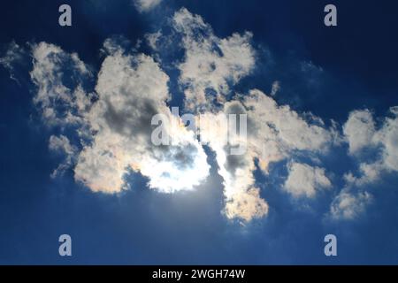 Looking straight up at a triangular cloud blocking the sun overhead, creating dramatic shadows and a bright silver lining Stock Photo