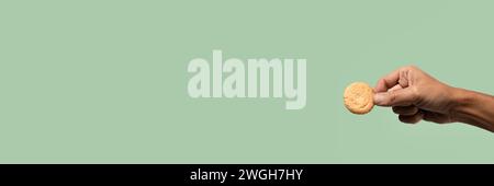 Male hand holding a biscuit on green background banner. Stock Photo