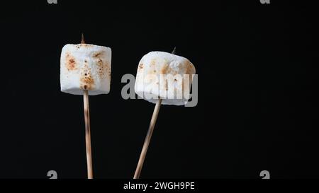 Bamboo sticks with two roasted marshmallow isolated  on black background Stock Photo