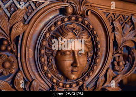 Elegant wood carving of a woman's face (possibly Marianne, symbol of France)  with intricate floral patterns on vintage furniture. Paris, France. Stock Photo