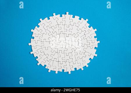 Plain white jigsaw puzzle  on blue color background, oval shaped frame, abstract backdrop Stock Photo