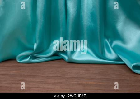 empty wooden floor with Elegant wavy turquoise satin cloth curtains, defocused in the background, product placement backdrop Stock Photo