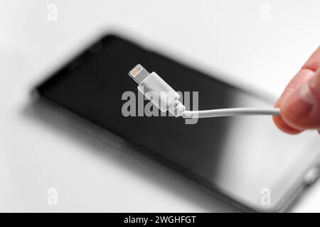 White broken cable with smartphone charging plug in hand close up. Black mobile phone in blur on a background Stock Photo