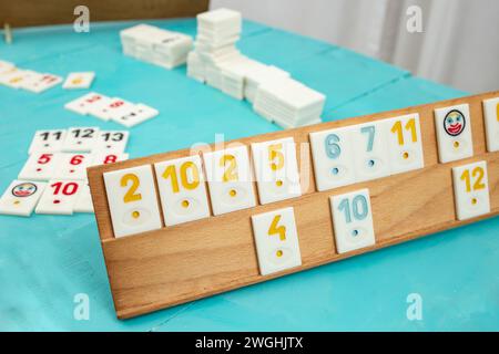 Plastic tiles from the game rummikub, rummicub or  okey in Turkey arranged on a wooden rack, on blue table background Stock Photo