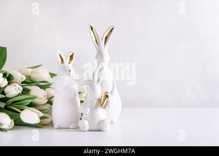 Three Easter rabbits figurines with bouquet of white tulips on white background. Easter celebration concept. Copy space. Front view Stock Photo