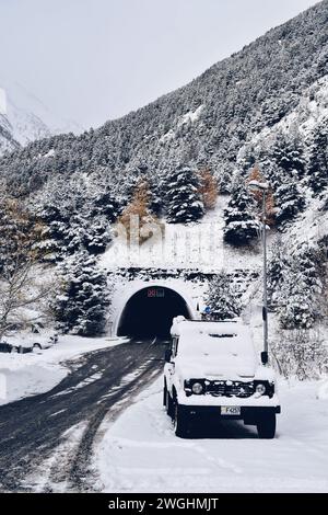 snowy road at the exit of a tunnel with a parked car completely covered in snow in Andorra, on December 4, 2021 Stock Photo