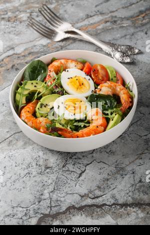 Mediterranean shrimp salad with avocado, arugula, spinach, tomatoes and boiled eggs close-up in a bowl on the table. Vertical Stock Photo