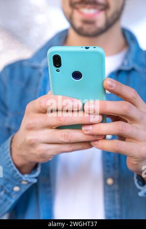 Vertical close-up unrecognizable Smiling young man using an app on his smartphone and standing outdoors. Stock Photo