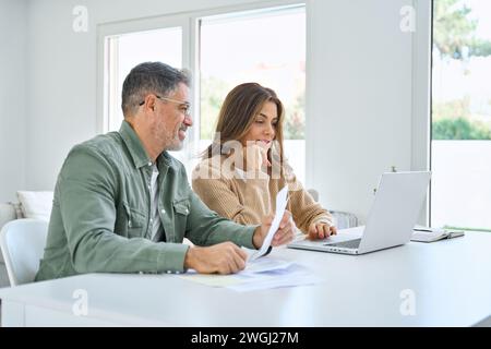 Happy middle aged mature man and woman couple paying bills online at home. Stock Photo