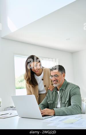 Happy mature older couple using laptop technology at home. Vertical candid shot. Stock Photo