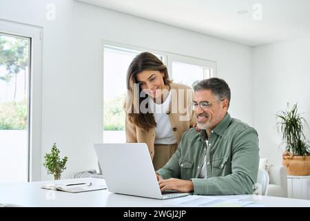 Happy middle aged couple using laptop technology at home. Authentic shot. Stock Photo