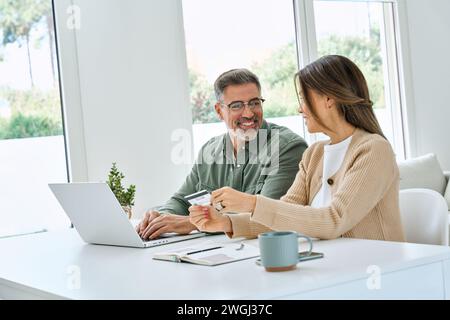 Happy mid aged couple using laptop computer holding credit card buying online. Stock Photo