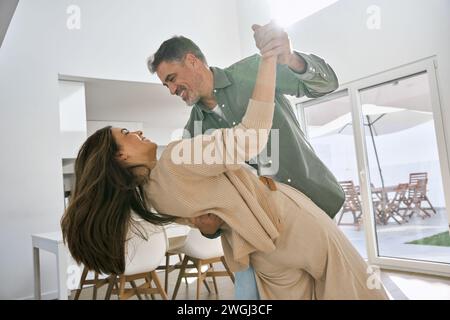 Happy affectionate loving middle aged mature couple dancing at home in kitchen, Stock Photo