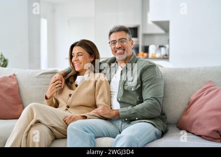Happy middle aged mature romantic couple hugging sitting on couch at home. Stock Photo