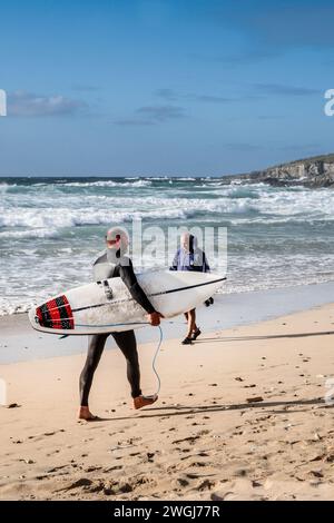 A surfer carrying his surfboard walking along the shoreline on the iconic Fistral Beach in Newquay in Cornwall in the UK. Stock Photo
