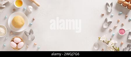 Easter banner. Concept preparation and homemade cook with raw dough, ingredients, cookie cutters, eggs on baking white background. Top view. Greeting Stock Photo
