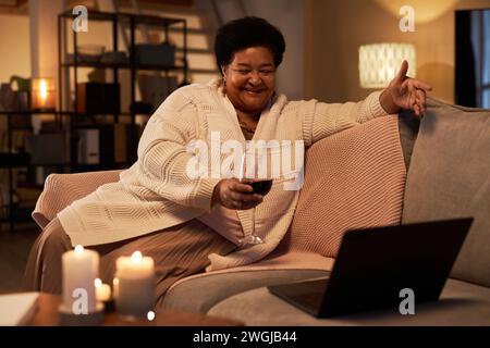 Portrait of mature Black woman smiling while enjoying conversation via video chat with glass of wine at home copy space Stock Photo