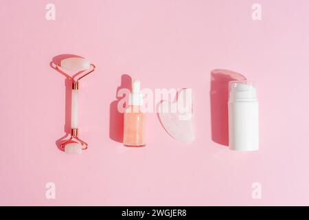 Cosmetic cream and serum bottles, facial roller and gua sha stone on pink background with shadows. Skin care concept. Top view, flat lay. Stock Photo