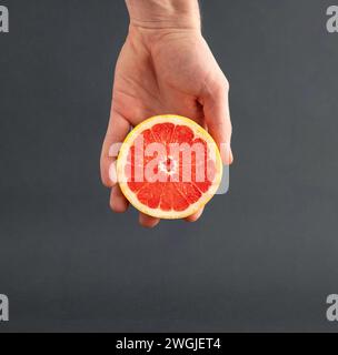 Sliced fresh grapefruit in man's hand on gray background. A source of vitamin C. Nutrition concept. Stock Photo