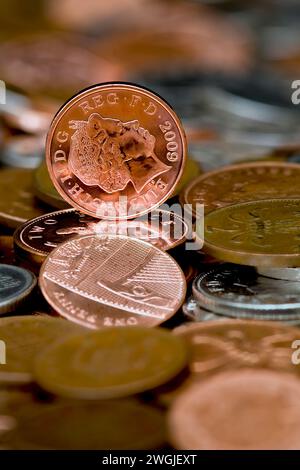 Studio shot of a one penny piece in Sterling currency standing upright on a table full of loose change with out of focus coins in foreground Stock Photo