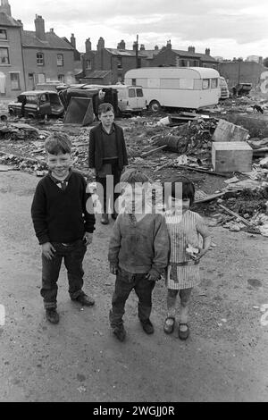 Irish Travellers children 1960s UK. Gypsy Irish travellers kids, their encampment on city centre wasteland Balsall Heath. Their caravan in background.  Parents and other tinkers are making money out of scrap metal – scrap cars. The houses are on Emily Street. Birmingham, England March 1968.  1960s UK  HOMER SYKES Stock Photo