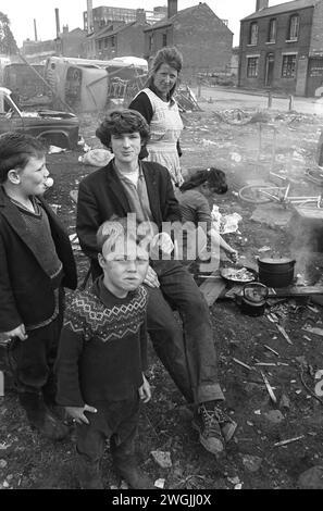 Gypsy Irish travellers family group, inner city encampment and temporary scrap car dump on waste ground in Balsall Heath. A family  cook an afternoon meal on an open fire.  The houses are on Emily Street. Balsall Heath, Birmingham, England March 1968.  1960s UK  HOMER SYKES Stock Photo