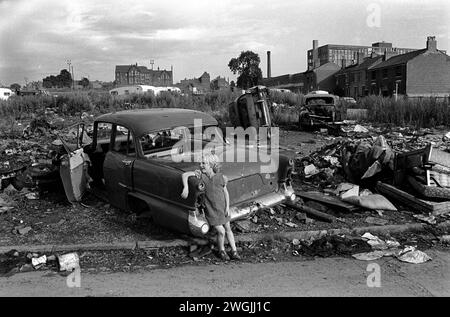 Gypsy Irish travellers encampment and temporary scrap car dump on waste ground in Balsall Heath, an inner city slum area. Young girl leaning on a scrap car scrap dump. Balsall Heath, Birmingham, England March 1968 1960s UK HOMER SYKES Stock Photo